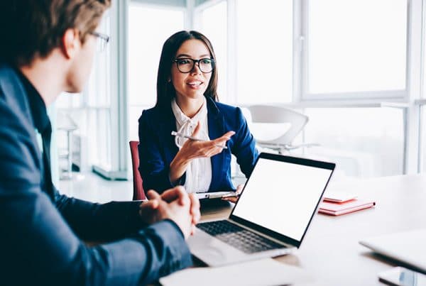 Businesswoman in blue blazer and glasses enhancing client relationships during meeting in windowed conference room.