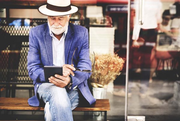 Older adult sitting on a bench reading on a tablet.