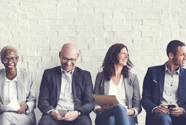 Row of professionals seated in front of a white brick wall.