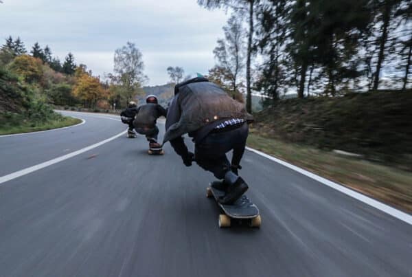 Three people skating on skateboards downhill with motion blue showing immense speed, surrounded by trees and hills.